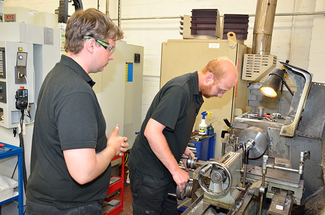 Some machining is still carried out on a manual lathe. Chief designer Sean does the work watched closely by recent recruit and Pit Bike racer Eliot.