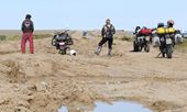 A group of motorcyclists look at a rutted road