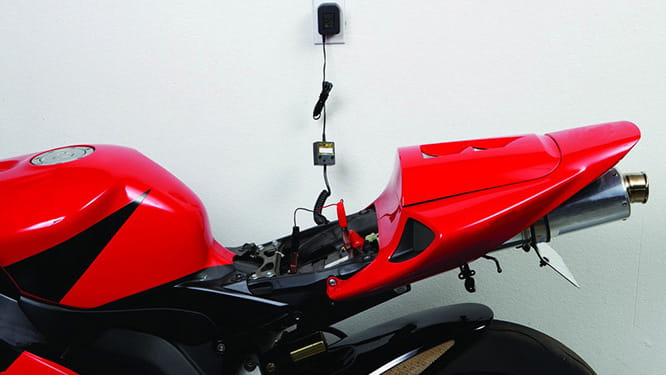  Red motorbike connected to a trickle charger during winter